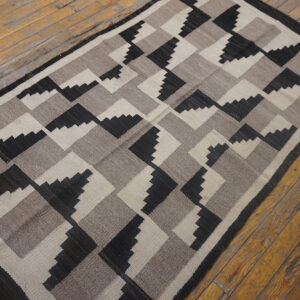 Black, taupe, and off-white flat weave rug with stepped geometric pattern on worn wood planks.