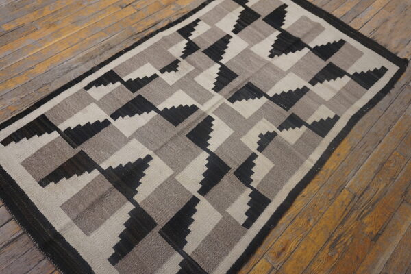 Black, taupe, and off-white flat weave rug with stepped geometric pattern on worn wood planks.