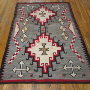 Flatweave rug with gray field, geometric patterns in red, white, black, and tan on distressed wood planks.