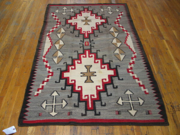 Flatweave rug with gray field, geometric patterns in red, white, black, and tan on distressed wood planks.