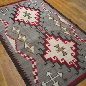 Gray geometric flatweave rug with red, white, black, and tan patterns rests on rustic wood flooring.