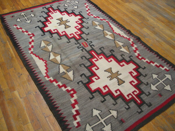 Gray geometric flatweave rug with red, white, black, and tan patterns rests on rustic wood flooring.