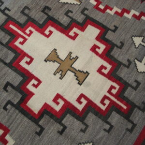 Geometric flat-woven rug featuring a gray ground, central white medallion, and striking red, black, and tan motifs.