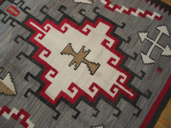 Geometric flat-woven rug featuring a gray ground, central white medallion, and striking red, black, and tan motifs.
