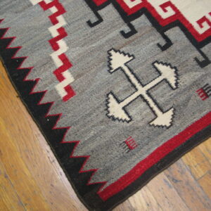 Geometric gray, red, and black flatweave rug featuring stepped cross motifs rests on wooden planks.