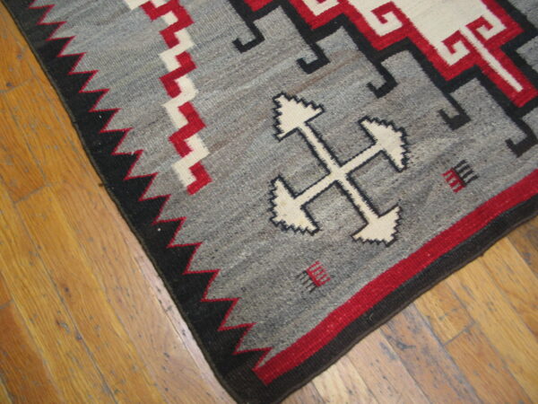 Geometric gray, red, and black flatweave rug featuring stepped cross motifs rests on wooden planks.