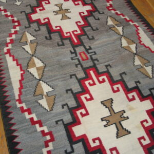 Low pile geometric rug in gray, white, red, and tan tones rests on light brown wood plank flooring.