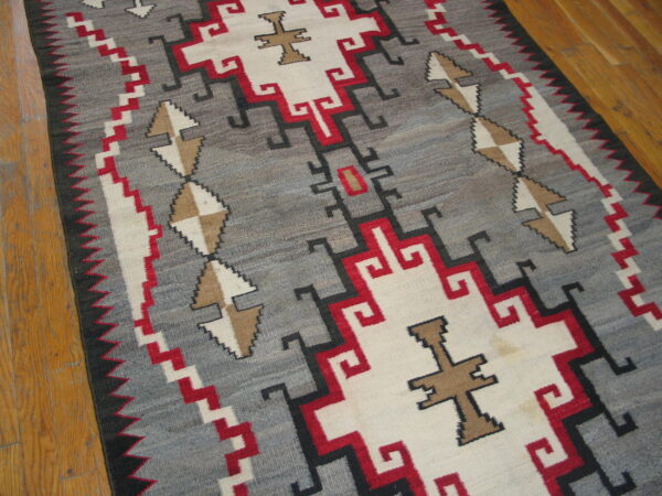 Low pile geometric rug in gray, white, red, and tan tones rests on light brown wood plank flooring.