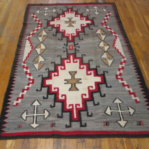 Geometric flatweave rug in grey, red, cream, and black tones displayed on polished wood floor.