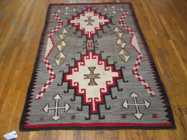 Geometric flatweave rug in grey, red, cream, and black tones displayed on polished wood floor.