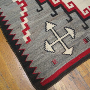 Flatweave rug in gray, red, white, and black geometric patterns rests on light wood planks.