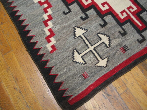 Flatweave rug in gray, red, white, and black geometric patterns rests on light wood planks.