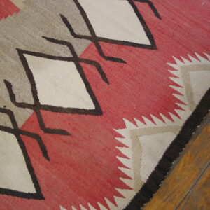 A flatweave rug features bold red, tan, and white diamonds outlined in dark brown on wood planks.