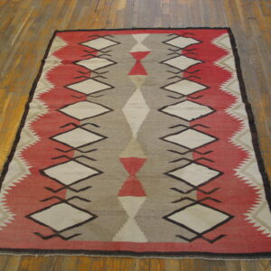 Geometric red, taupe, and cream flatweave rug with repeating diamond motifs on wood planks.