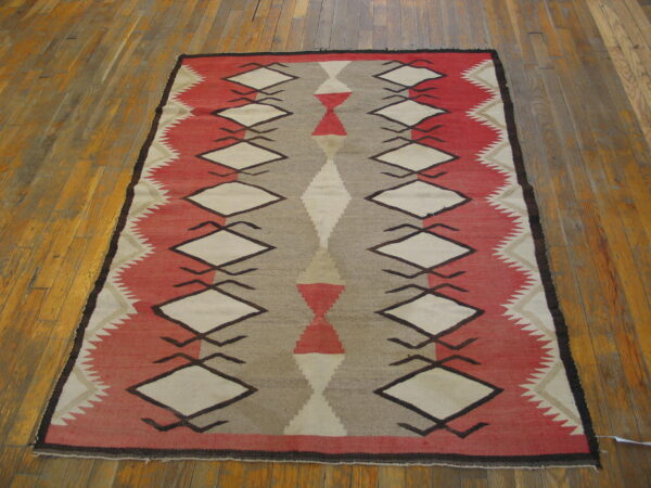 Geometric red, taupe, and cream flatweave rug with repeating diamond motifs on wood planks.