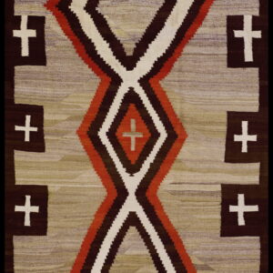 Flat woven rug with rust, brown, and cream hourglass shapes surrounded by crosses on a mottled tan field.
