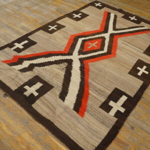 Geometric flatweave rug in beige, dark brown, orange, and cream rests on distressed wood flooring.