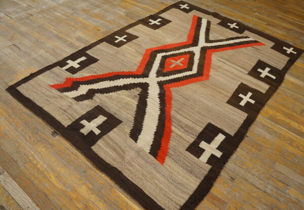 Geometric flatweave rug in beige, dark brown, orange, and cream rests on distressed wood flooring.
