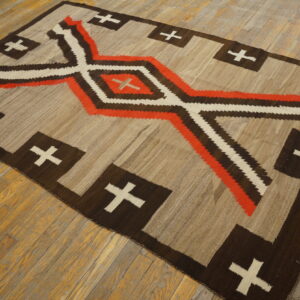Beige and brown flatweave rug with orange, white, and dark geometric patterns on worn wood floors.
