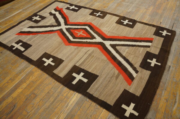 Beige and brown flatweave rug with orange, white, and dark geometric patterns on worn wood floors.