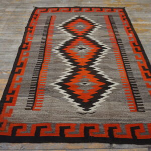 Gray and orange flatwoven rug with a zigzag diamond pattern, resting on distressed gray wood floorboards.