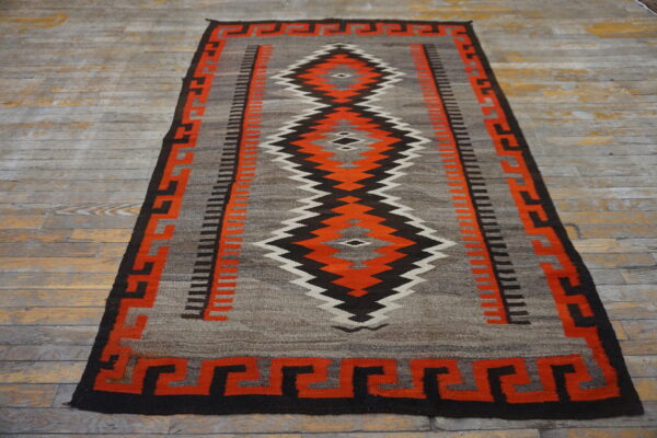 Gray and orange flatwoven rug with a zigzag diamond pattern, resting on distressed gray wood floorboards.
