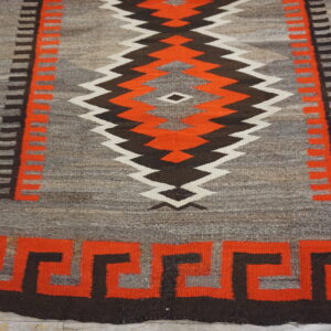Low-pile geometric rug in gray, red-orange, brown, and white on distressed wood flooring.