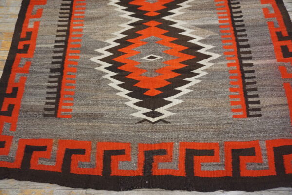 Low-pile geometric rug in gray, red-orange, brown, and white on distressed wood flooring.