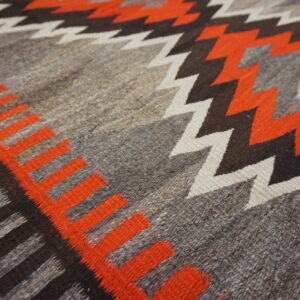 Low-pile rug detail showing natural gray, orange, dark brown, and white geometric zigzag and diamond patterns.