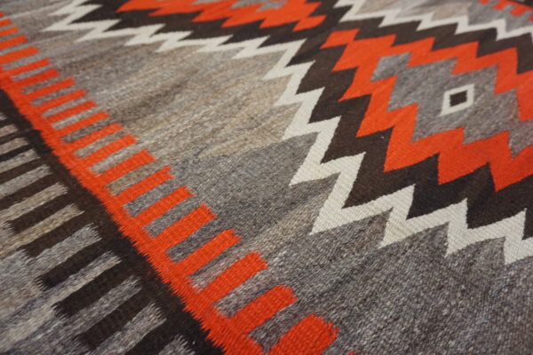 Low-pile rug detail showing natural gray, orange, dark brown, and white geometric zigzag and diamond patterns.