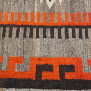 Close-up of flatweave rug featuring interlocking orange and black geometric designs on a mixed gray background.