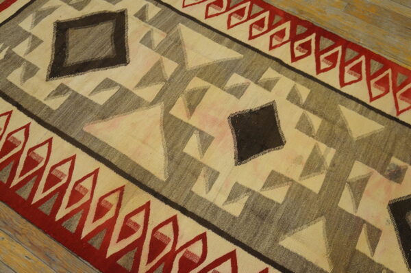 Flatweave rug with geometric diamonds and zigzags in cream, red, and dark gray on wood planks.