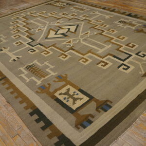 Square rug with a geometric tribal design in muted earth tones on distressed hardwood flooring.