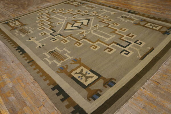 Square rug with a geometric tribal design in muted earth tones on distressed hardwood flooring.