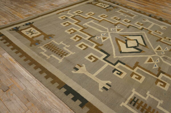 Geometric flatweave rug in gray, cream, brown, and blue rests on rustic light wood flooring.