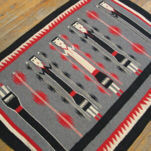 Flatwoven rug on wood floor with gray field, black figures, red accents, and zigzag borders.