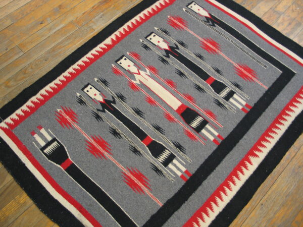 Flatwoven rug on wood floor with gray field, black figures, red accents, and zigzag borders.