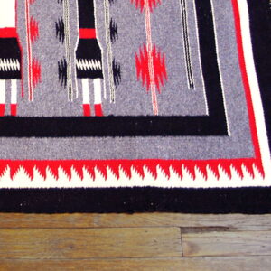 Flat weave rug in gray, black, white, and red with vertical figures and stepped borders on wood floor.