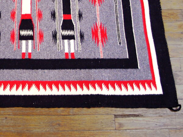 Flat weave rug in gray, black, white, and red with vertical figures and stepped borders on wood floor.