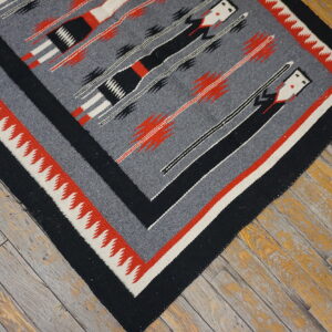 Gray, black, red, and cream patterned flatweave rug resting on weathered wood planks.