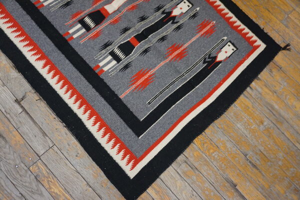Gray, black, red, and cream patterned flatweave rug resting on weathered wood planks.
