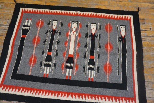 Low-pile rug displaying stylized black, white, and red figures on a gray background atop wood flooring.