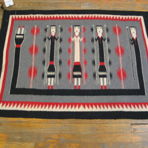 Rectangular rug in gray, black, red, and white with stylized figures visible on wood flooring.
