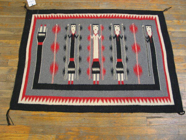 Rectangular rug in gray, black, red, and white with stylized figures visible on wood flooring.