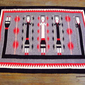 Black, gray, red, and white rug with abstract human figures and geometric motifs on wood flooring.