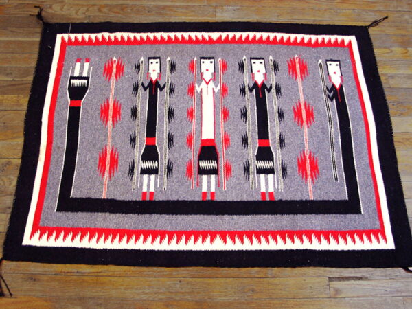 Black, gray, red, and white rug with abstract human figures and geometric motifs on wood flooring.