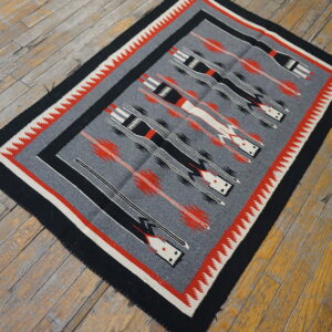 A gray flatweave rug with black, red, and white geometric patterns rests on rustic wood floors.
