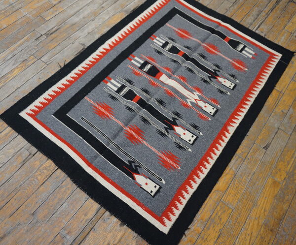 A gray flatweave rug with black, red, and white geometric patterns rests on rustic wood floors.