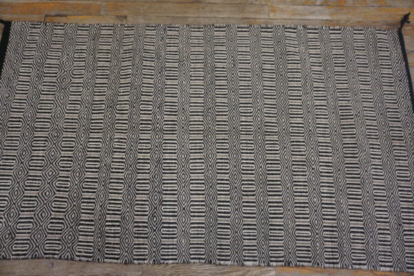 Textured gray and black rug with repeated diamond and elongated hexagon motifs shown on hardwood.