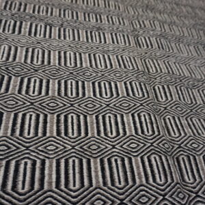 Black and shades of gray geometric rug featuring repeating oblong and diamond shapes on wood flooring.
